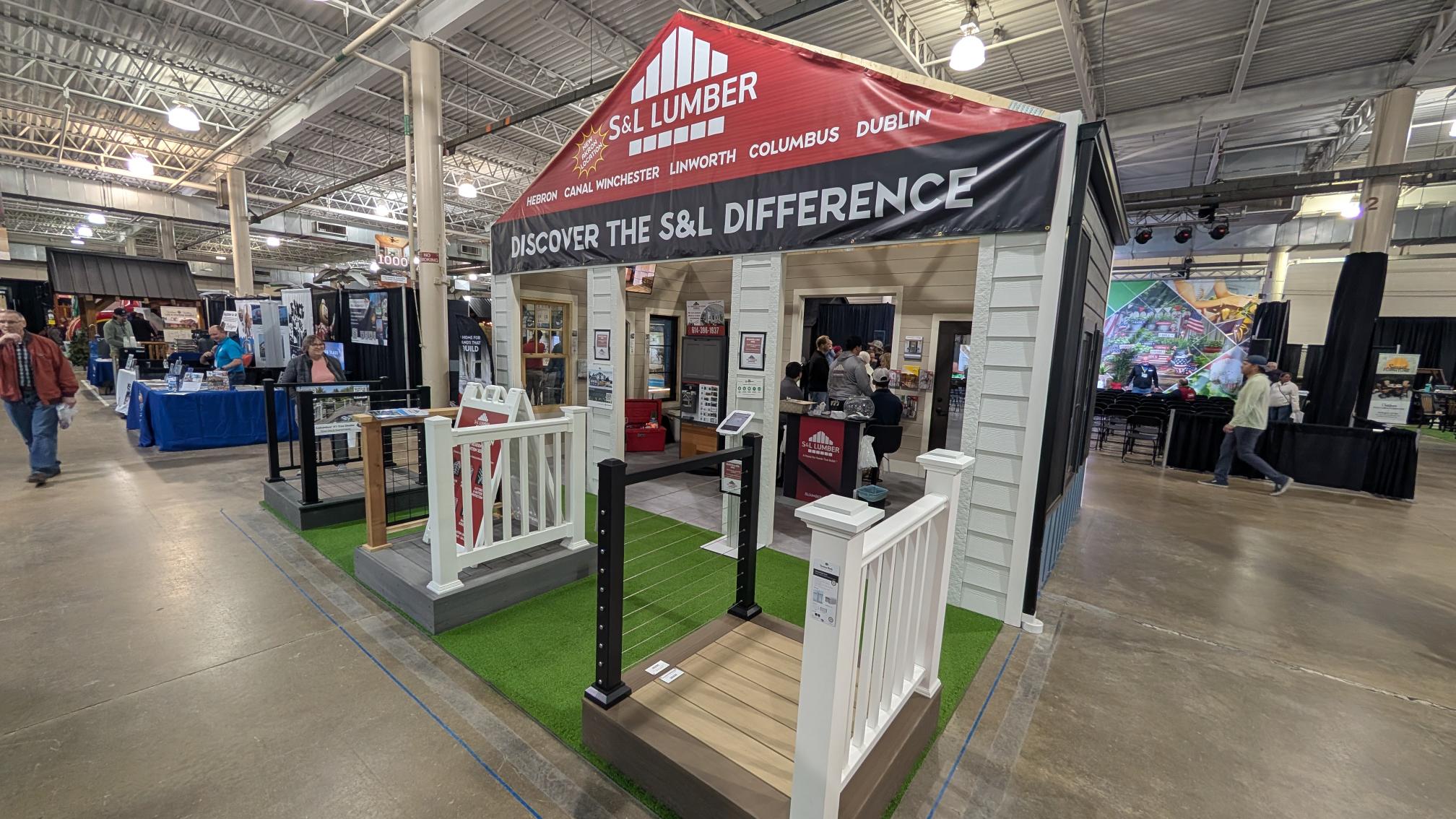 Indoor expo booth for S&L Lumber with a white porch display on green turf and a large banner: Discover the S&L Difference.